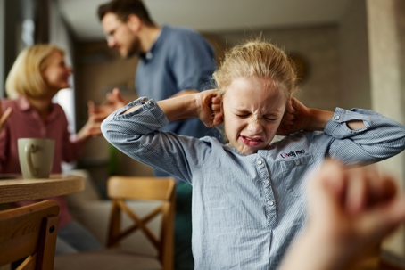 child frustrated with parents fighting in the background